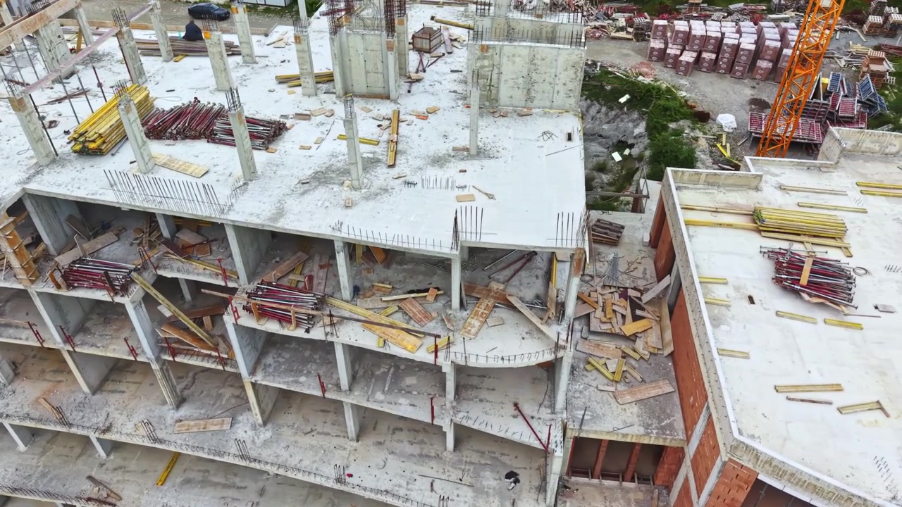 El sitio presenta una construcción actual con trabajadores y equipos presentes. Una perspectiva aérea captura el desarrollo de hormigón curvo con andamios y trabajadores activamente involucrados