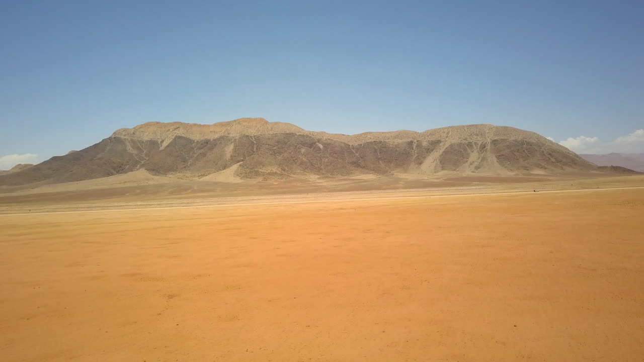 4K drone footage flying toward a towering rock formation in Namibia’s vast desert. The landscape features striking yellow-orange sand, creating a stunning contrast with the rugged terrain.