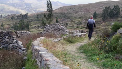 young caucasian man walks amid abandoned stone ruins of uyo uyo, peru