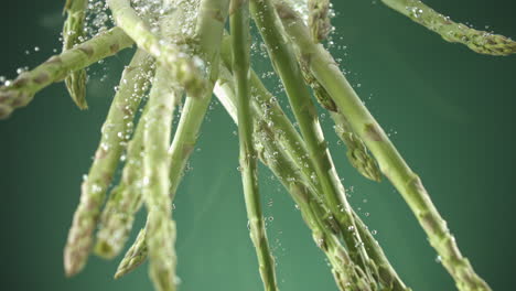 slow motion of fresh raw asparagus falling into water on green background