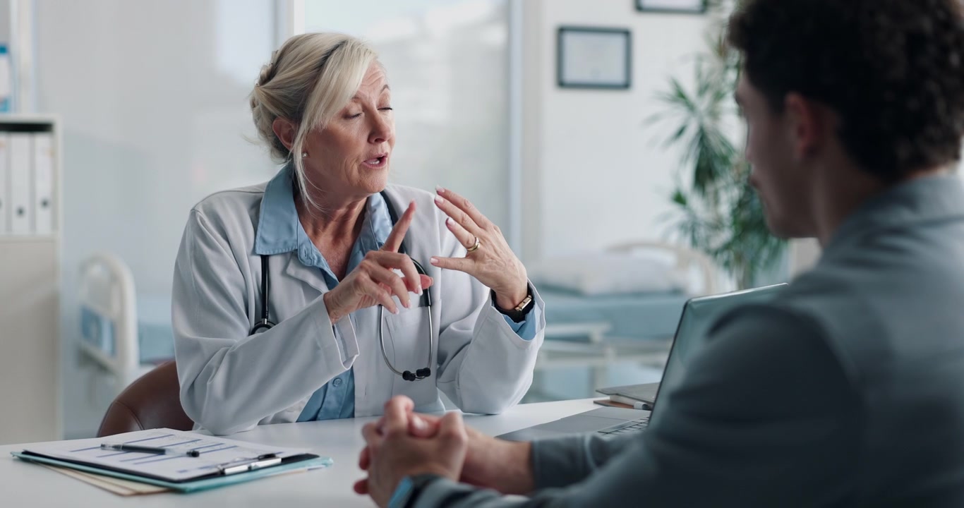Senior Female Doctor Consulting with Male Patient in Medical Office