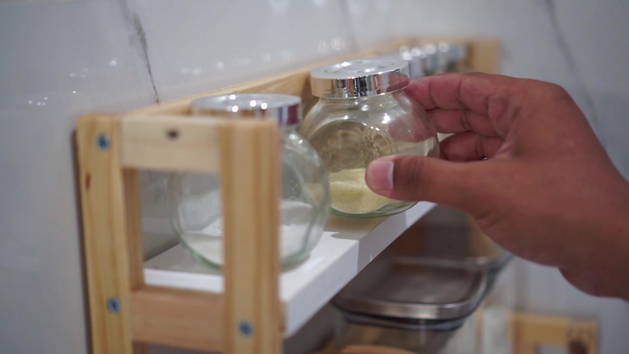 Primer plano de una mano colocando un recipiente de caldo en polvo de nuevo en el estante, concepto de organización de cocina, almacenamiento de ingredientes y hogar