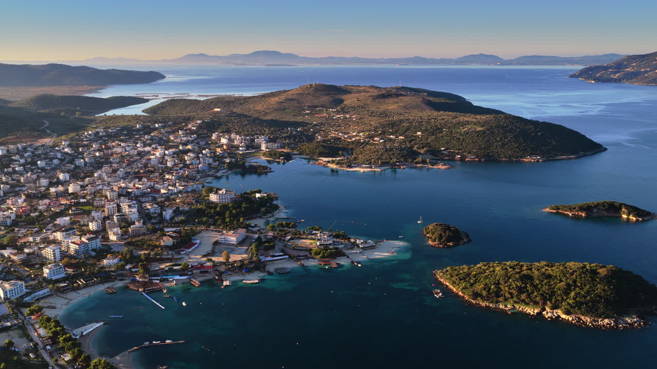 Aerial drone view of Ksamil town, it's dense cluster of hotels and houses, and the iconic bright blue bays with floating platforms and beach clubs