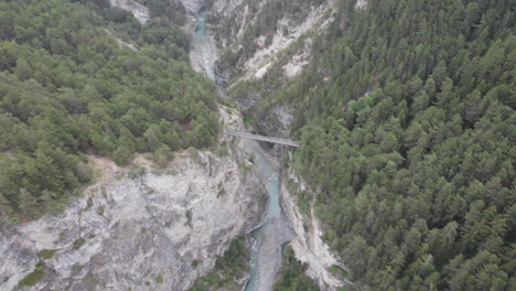 aerial drone shot flying over tilting down tracking a suspension bridge which joins two cliffs of a deep valley gorge together with the arc river flowing below in aussois, france