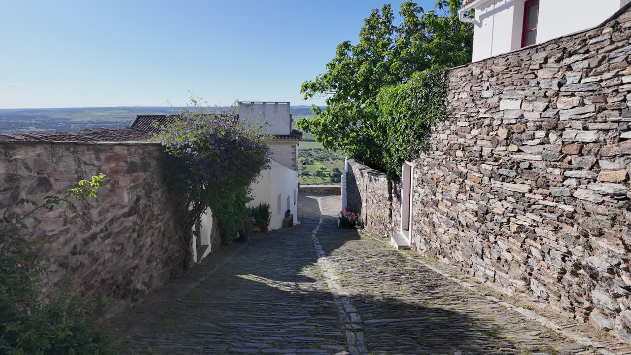 Sunlit narrow street lined with stone walls in Monsaraz Portugal