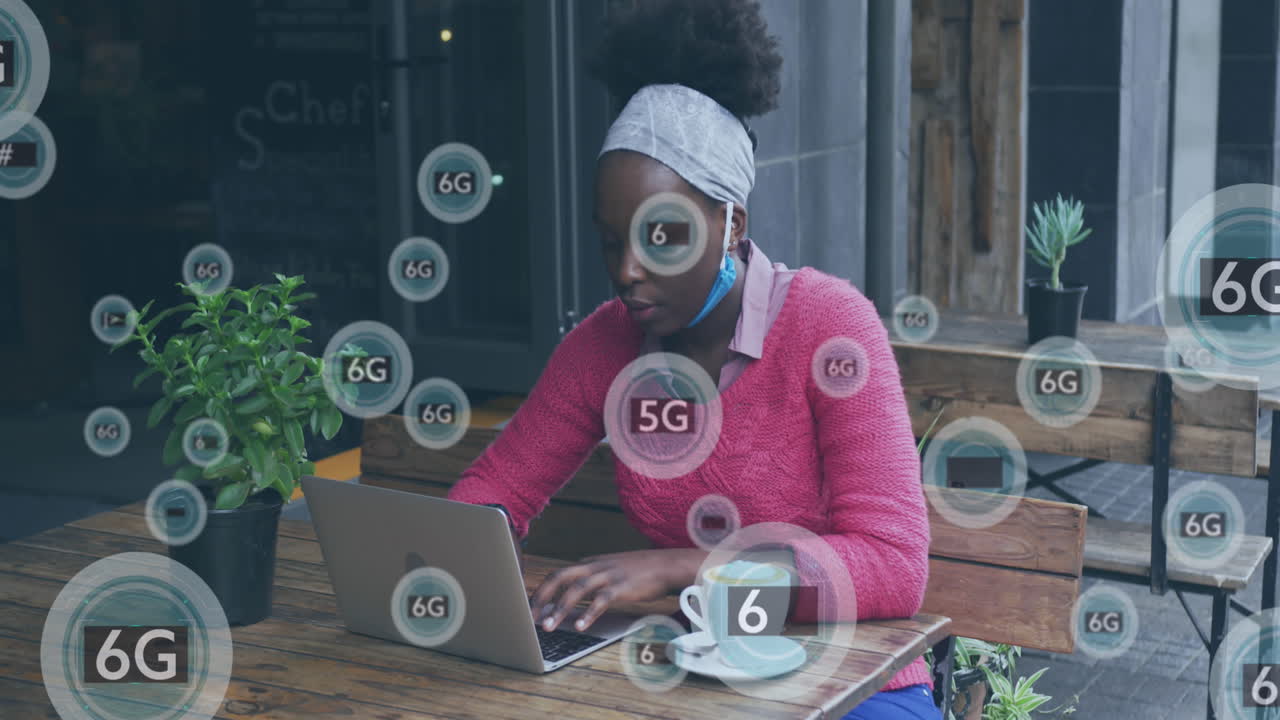 Animation of 5g and 6g icons over african american woman using laptop outside cafe