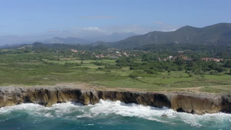 Panoramic-aerial-of-blue-crashing-waves-against-sea-cliffs-bufones-de-pria-asturias-spain