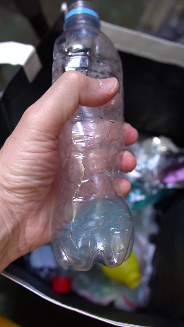 Manual compressing of clear plastic bottles by a hand into a recycling bin, sustainable waste concept