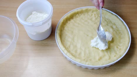 Female hands put cottage cheese on raw dough for homemade cake on kitchen table