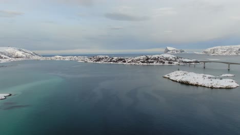 drone view in tromso area in winter flying over snowy islands next a bridge connecting white islands in norway