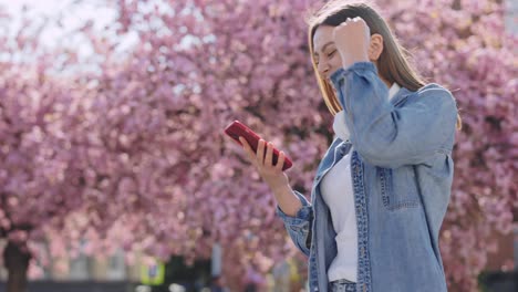 happy woman using phone outside among pink flowers