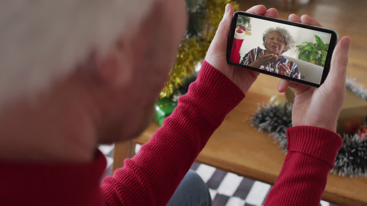 hombre caucásico con sombrero de santa usando un teléfono inteligente para una videollamada de navidad con una mujer sonriente en la pantalla