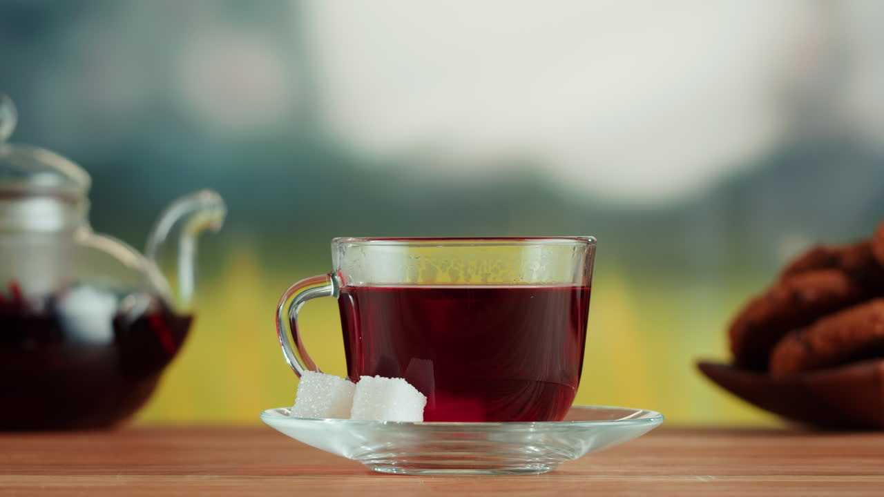 A hand adding a sugar cube to a cup of red tea