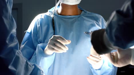 Diverse-surgeons-wearing-surgical-gowns-operating-on-patient-in-operating-theatre,-slow-motion