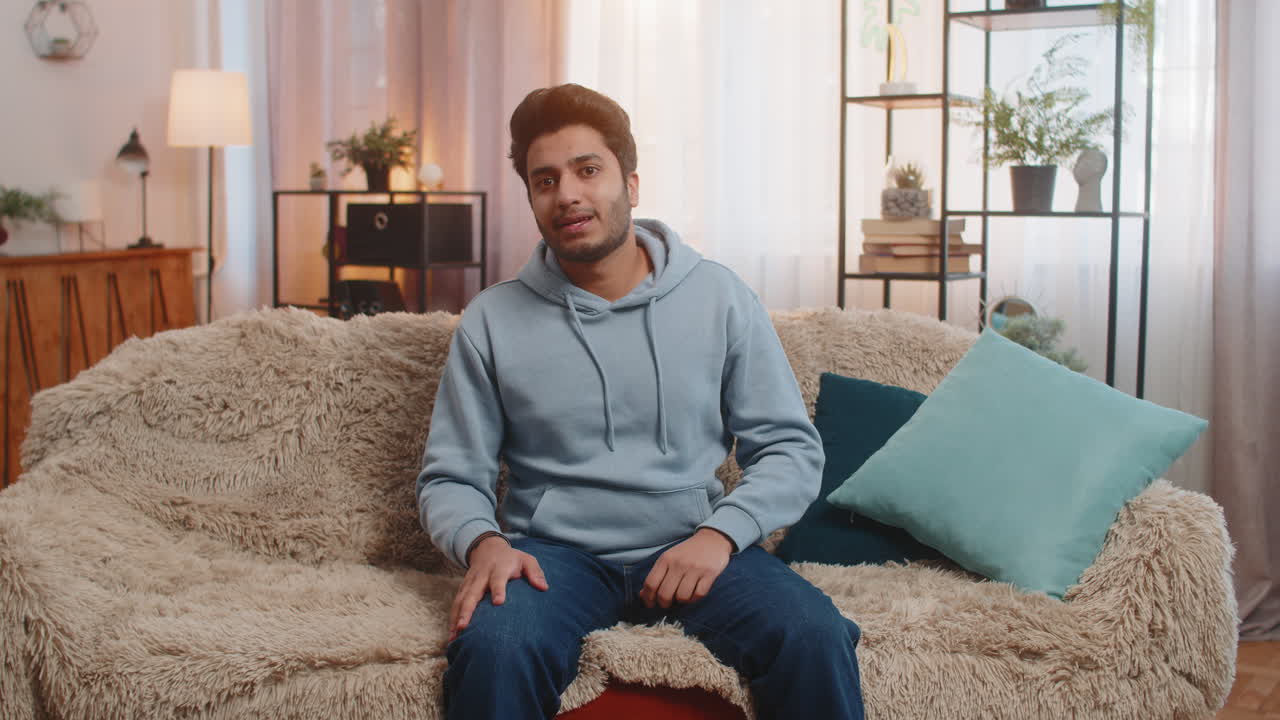 Cheerful indian young man smiling and waving hello while making video conference call at home
