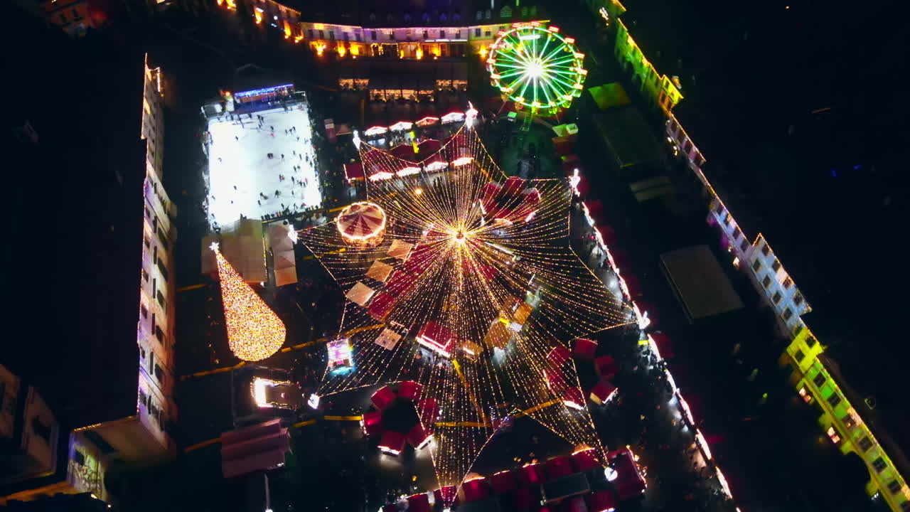 Aerial drone view of The Big Square in Sibiu at night, Romania. Old city centre decorated for Christmas. Ferris wheel, skating rink, people