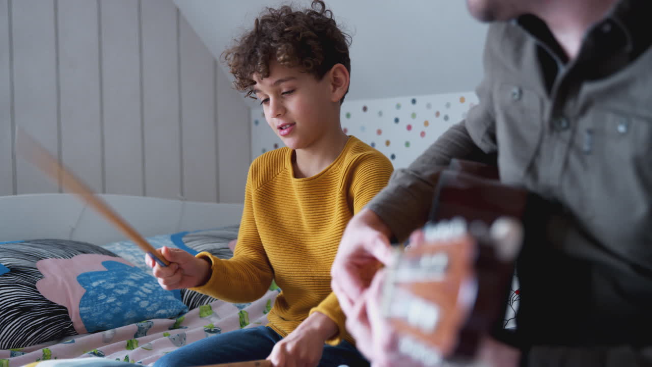 padre soltero tocando la guitarra con su hijo que toca la batería en el cojín en el dormitorio