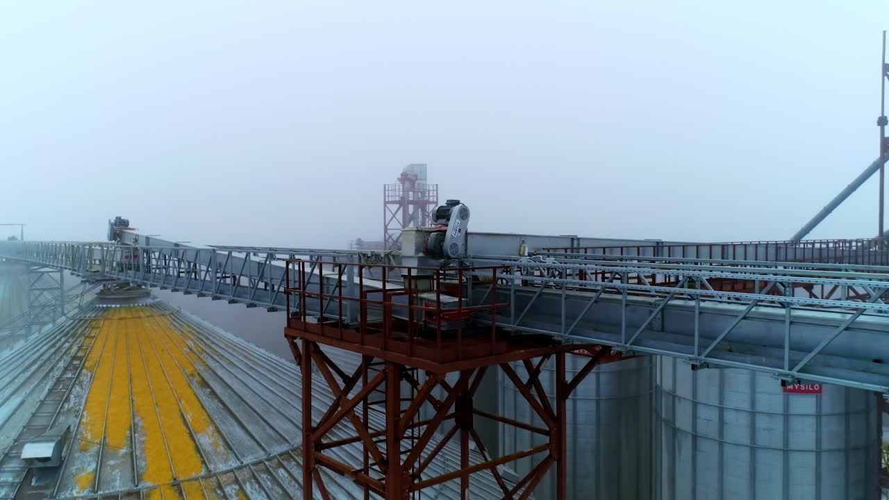 Metal beams on the tops of silo tanks joining them together. Moving along the beams in foggy weather. Misty air in the backdrop.