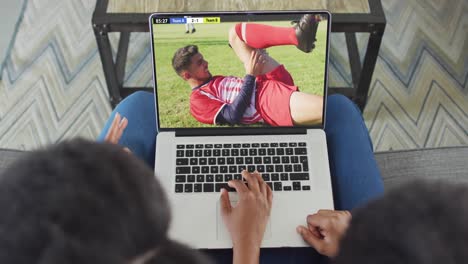 video de una pareja afroamericana sentada en el sofá y viendo fútbol en la computadora portátil en casa
