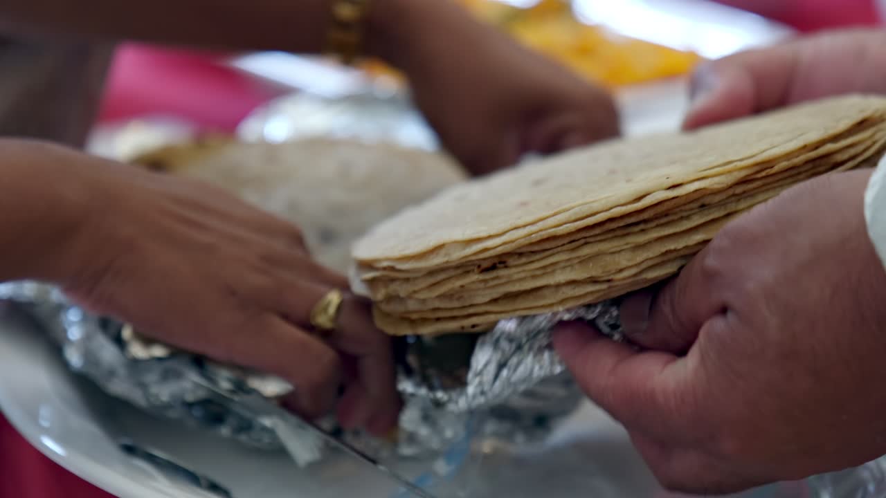 Hands carefully unwrap warm chapati from foil at an Indian wedding buffet. Traditional flatbread preparation scene capturing authentic Indian cuisine and festive catering
