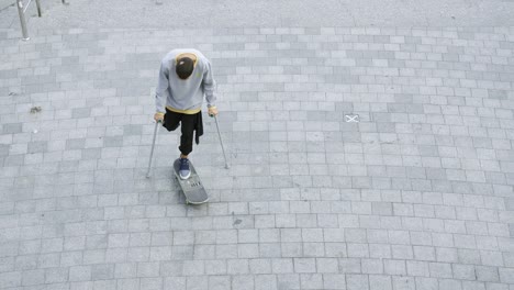 vista superior del hombre con una pierna en muletas girando en su patineta haciendo trucos.