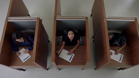 three women taking a test or filling out forms in individual booths
