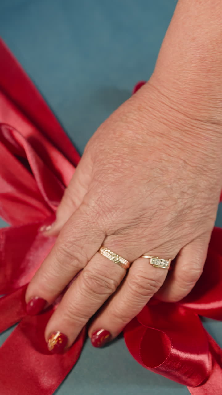 Hands of woman tying satin red ribbon on blue paper present box with surprise at home. Secret gift prepared for wedding anniversary closeup