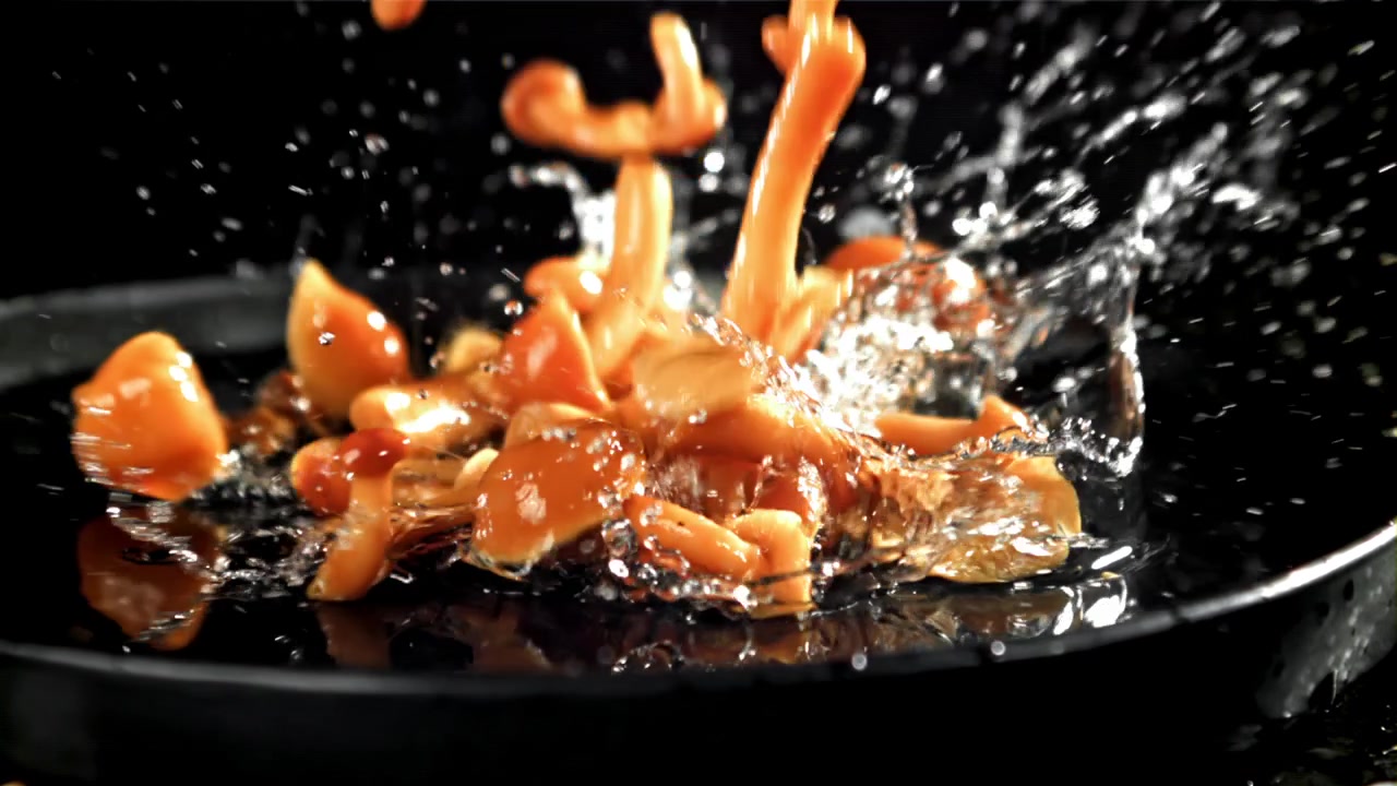 Friske svampe falder og sprøjter ned i en pande i slowmotion.