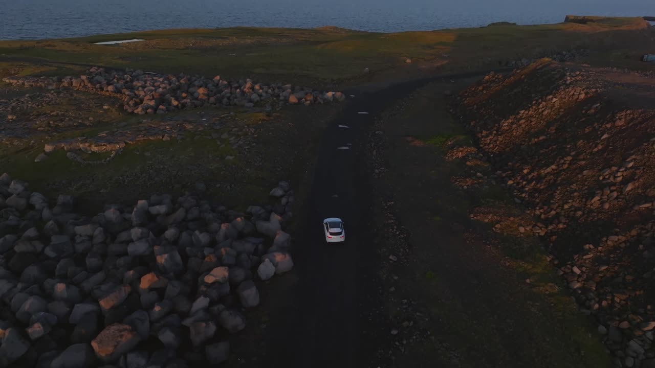 Bir araç, parlak bir işaret ışığına doğru engebeli bir yolda ilerliyor. Keflavik, Reykjanesbær.