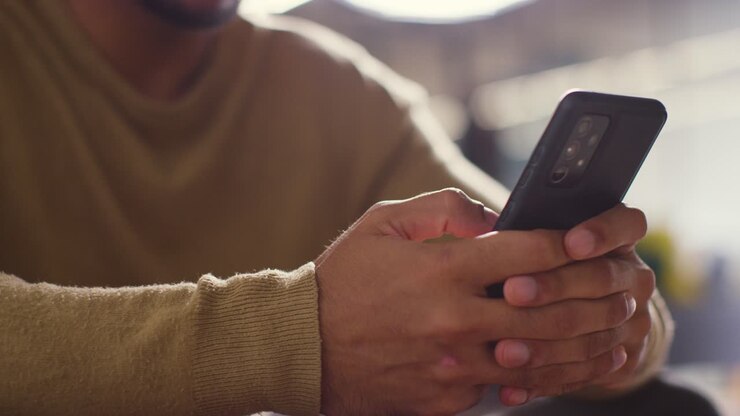 Primo piano di uomo musulmano a casa che tiene in mano un cellulare e scorre 1
