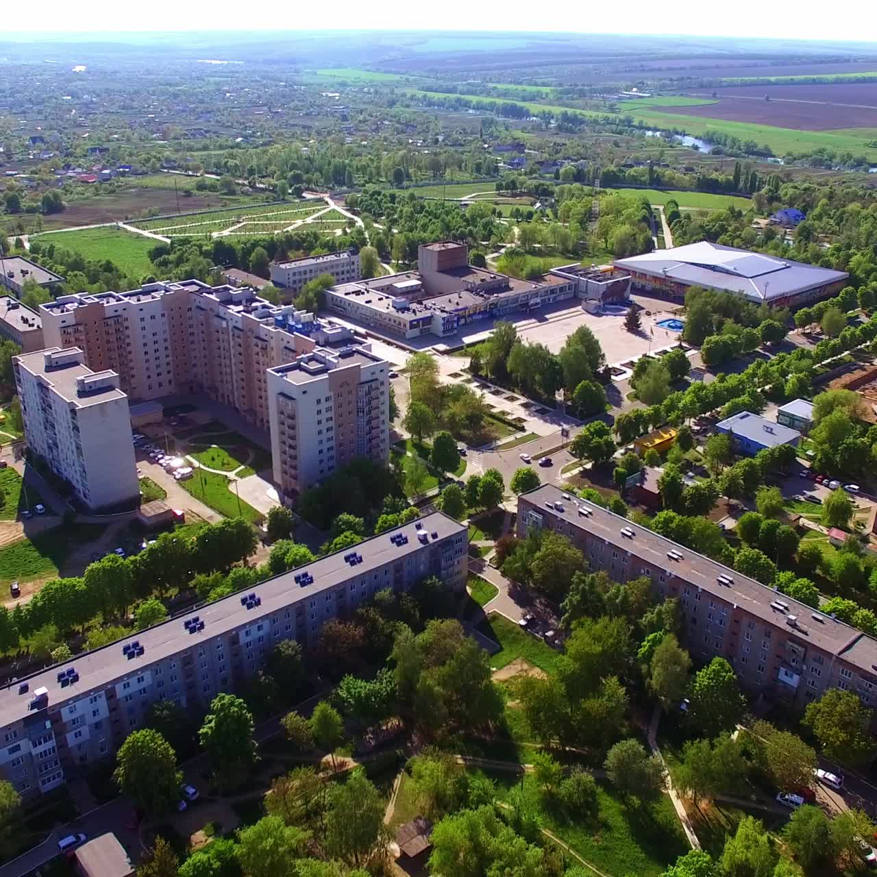Panorama ensolarado de uma cidade com prédios e ruas arborizadas. Território rural e fazendas ao fundo