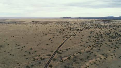 amplia antena mientras el coche conduce por la carretera en un desierto cubierto de matorrales cerca de wupatki, 4k