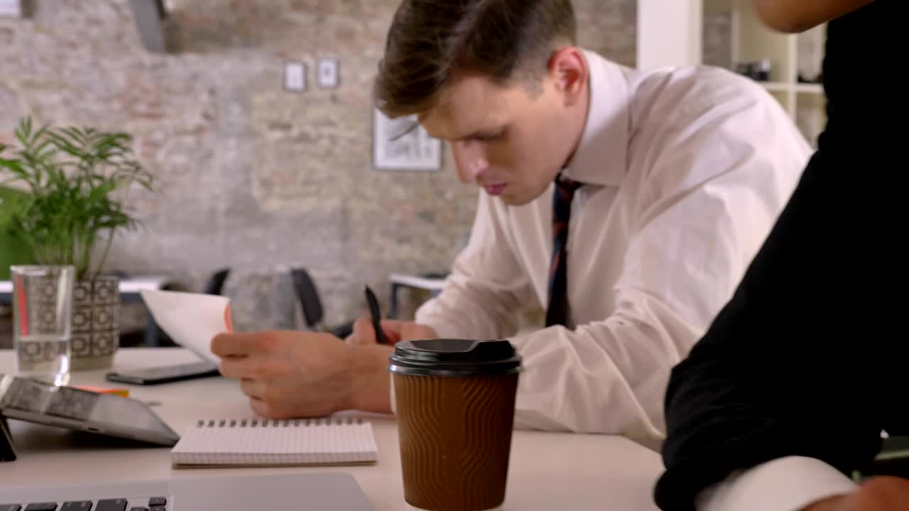 Team aziendale multietnico che lavora in un ufficio moderno, scrive su carta, un uomo di colore guarda il laptop, la telecamera avanza