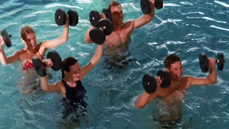 fit people doing an aqua aerobics class in swimming pool with foam dumbbells