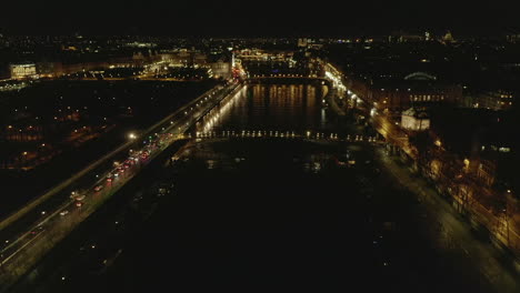 Forwards-fly-above-Seine-river-in-city-centre-at-night.-Illuminated-streets-and-waterfront,-lights-reflecting-on-water-surface.-Paris,-France