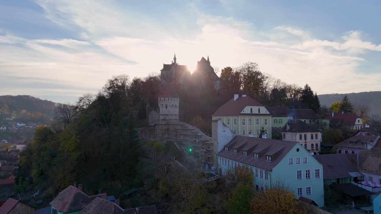 The camera glides over the historic city, showcasing its iconic towers, colorful buildings, and the prominent church, all set against the backdrop of vibrant autumn foliage.