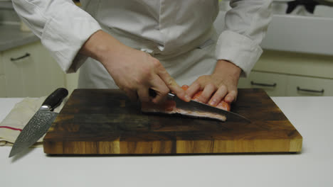 chef preparando salmón fresco en tabla de madera, cortando con cuchillo, de cerca