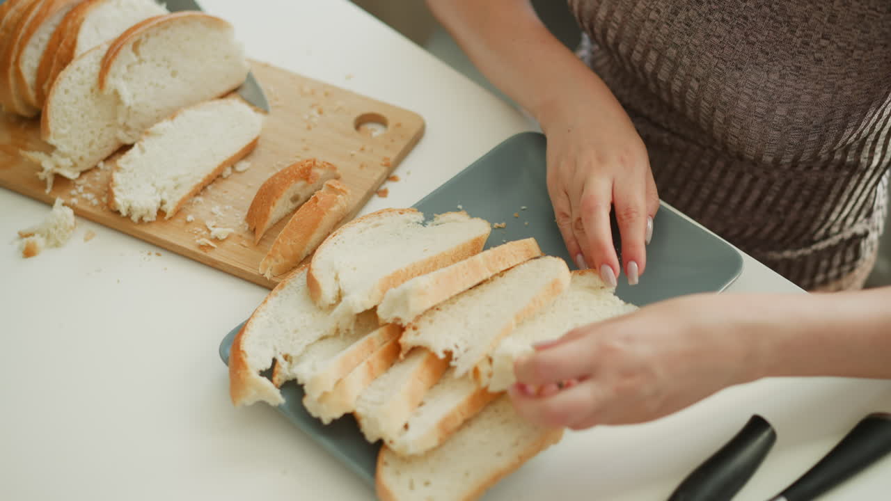 Hand view of baker placing sliced cake on tray on white table, focused on careful process under soft daylight, crumbs on wooden board and utensils nearby emphasize artisanal preparation scene