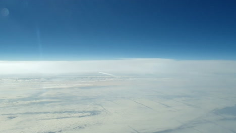 incredible view from the cockpit of an airplane flying high above the clouds leaving a long white condensation vapour air trail in the blue sky