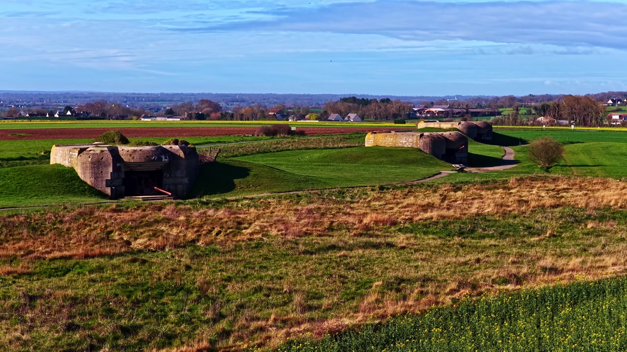 Aerial view of the Longues-sur-Mer Battery in Normandy, France, showing preserved World War II gun casemates set in open fields under clear coastal light.