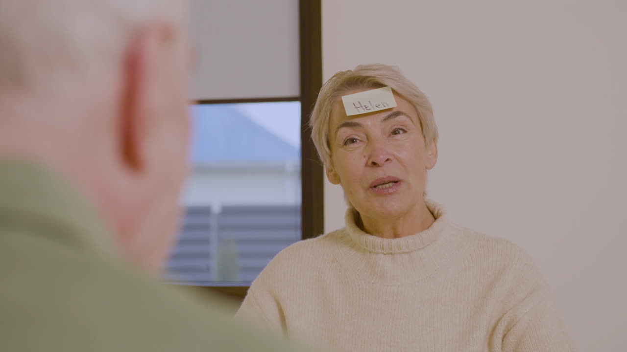 Happy Senior Woman Playing Guess Who Game With Sticky Papers Attaching On Forehead 1