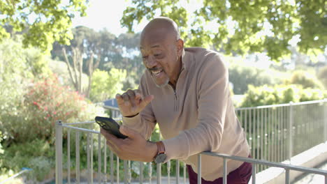 Happy-senior-biracial-man-using-smartphone-at-balcony-at-home,-slow-motion