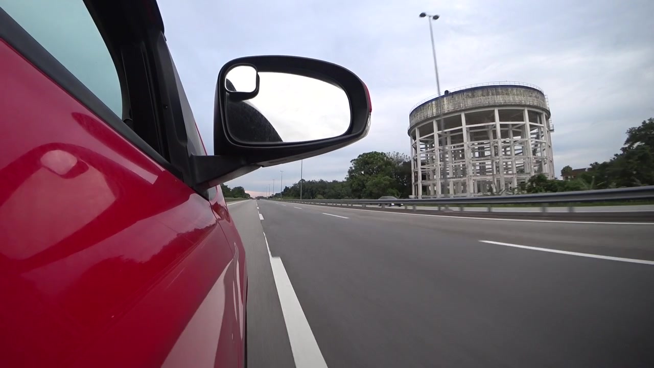 Ripresa panoramica di guida su un'autostrada tropicale tranquilla. Catturata da un supporto laterale esterno che mostra parte della carrozzeria dell'auto. Un viaggio tranquillo circondato da una natura lussureggiante e verde