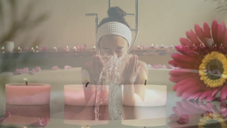 animation of pink flower and candles over happy biracial woman splashing face in bathtub