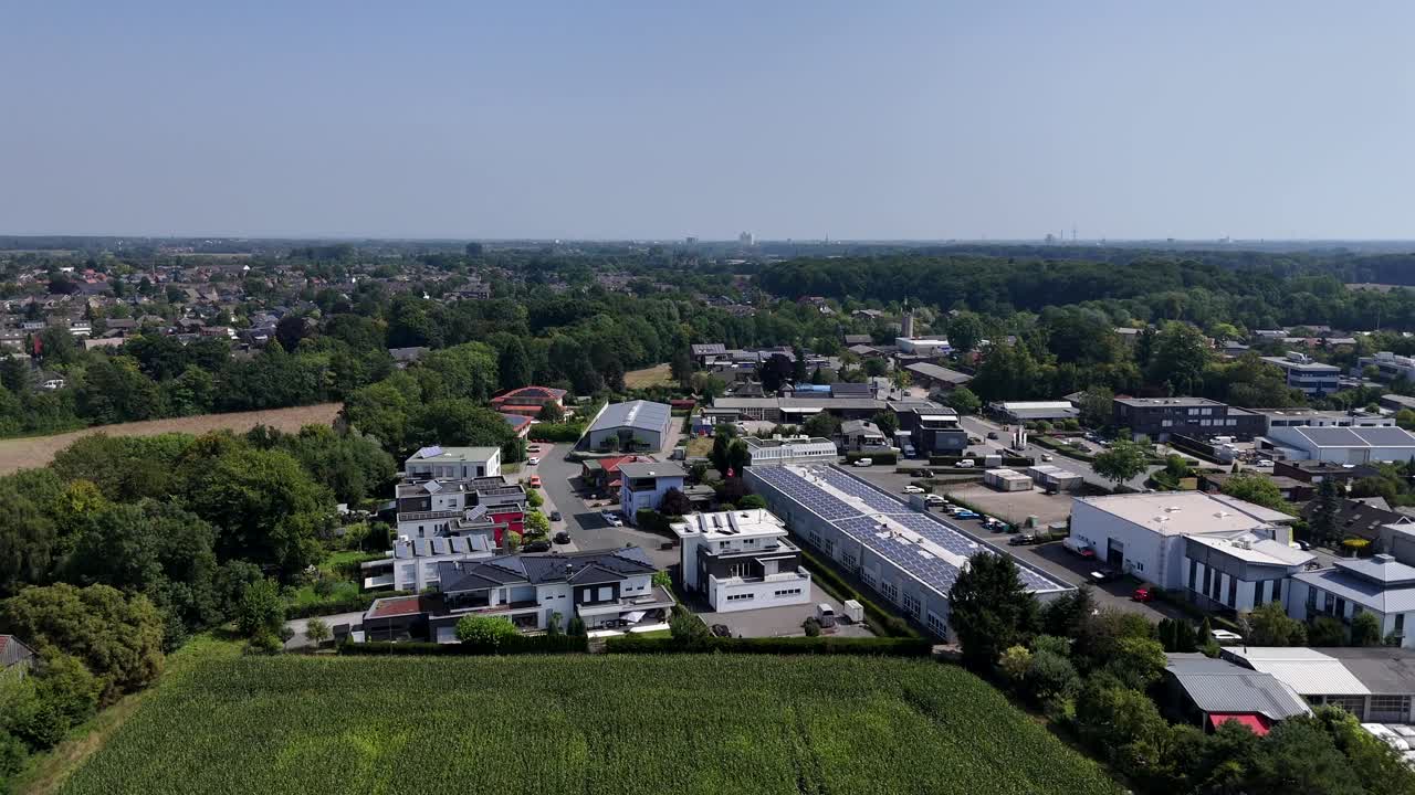 Modern houses and warehouse with solar panels near rural cultivated fields in America. Aerial forward wide shot. Sunny summer day. Industrial district with neighborhood