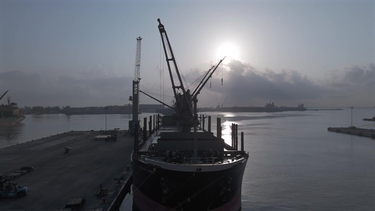 Cargo ship and dockside cranes at Port of Veracruz beneath hazy morning sunlight, aerial medium orbit descend