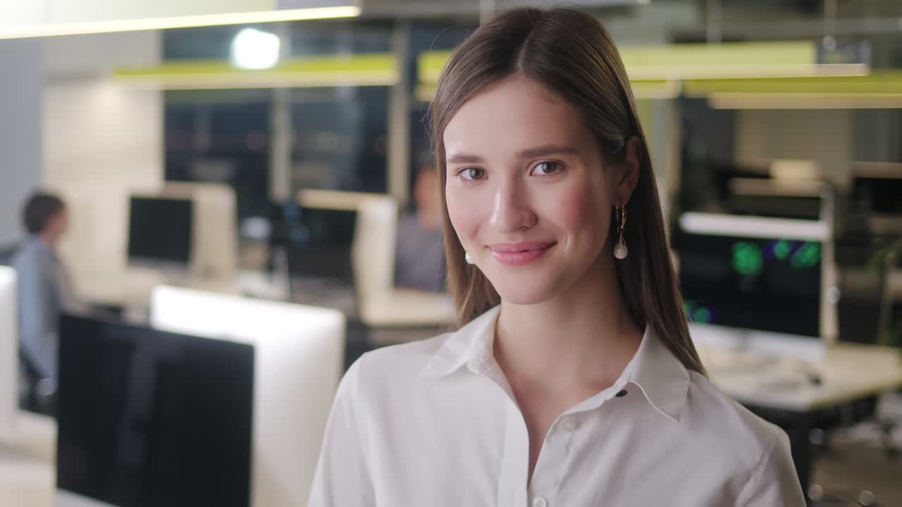 передний вид красивой молодой женщины в профессиональной белой рубашке. портрет молодой женщины-менеджера офиса, глядящей в камеру и имеющей хорошее настроение. размытый офисный фон