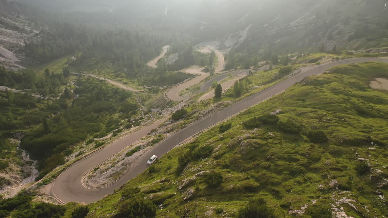 White car driving down winding mountain road in Italy, static aerial