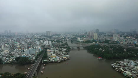 Ho-Chi-Minh-City,-Vietnam-morning-drone-flying-in-over-junction-of-Kenh-Te,-Ong-Lon-and-Ben-Nghe-canals,-working-river-boats-and-district-four-and-eight-waterfront-architecture,-rooftops-and-bridges