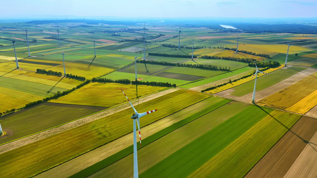 Wind turbines stand tall in green fields. Expansive view of wind turbines across vibrant agricultural fields on a sunny day, showcasing renewable energy